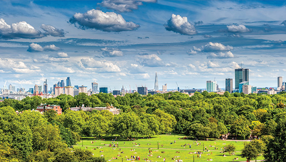 a panoramic view of a green park with numerous people enjoying outdoor activities in the foreground and a city skyline with tall buildings in the background featuring beautiful clouds and blue skies in a vibrant setting perfect for a seven wonders experience